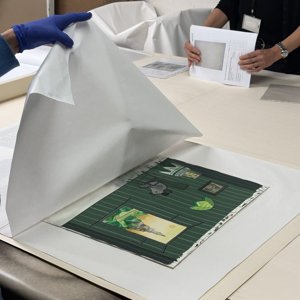 Jasny stół. Na stole leży kolorowa karta. Dłoń po lewej stronie podtrzymuje papier ochronny.