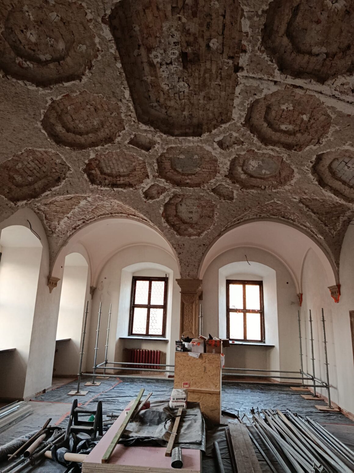 10 Wnętrze zabytkowego pomieszczenia o dekoracyjnym suficie. Na podłodze ułożone metalowe pręty.