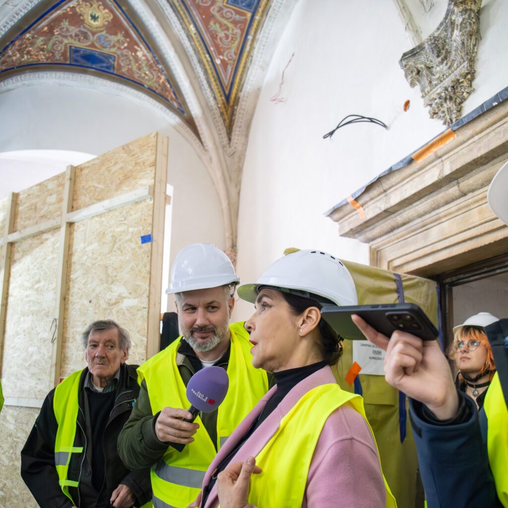 Kilka osób w białych kaskach i odblaskowych kamizelkach.