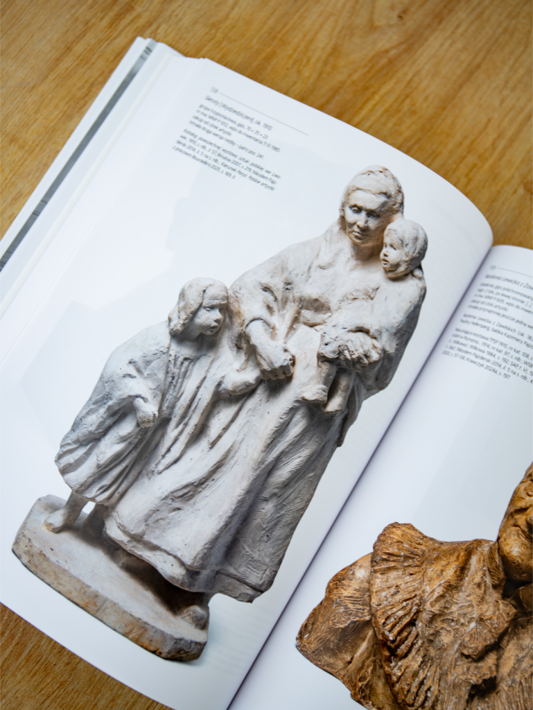 Fragment otwartej książki. Na stronie zdjęcie rzeźby matki z dwójką małych dzieci. Po prawej nieczytelny napis.