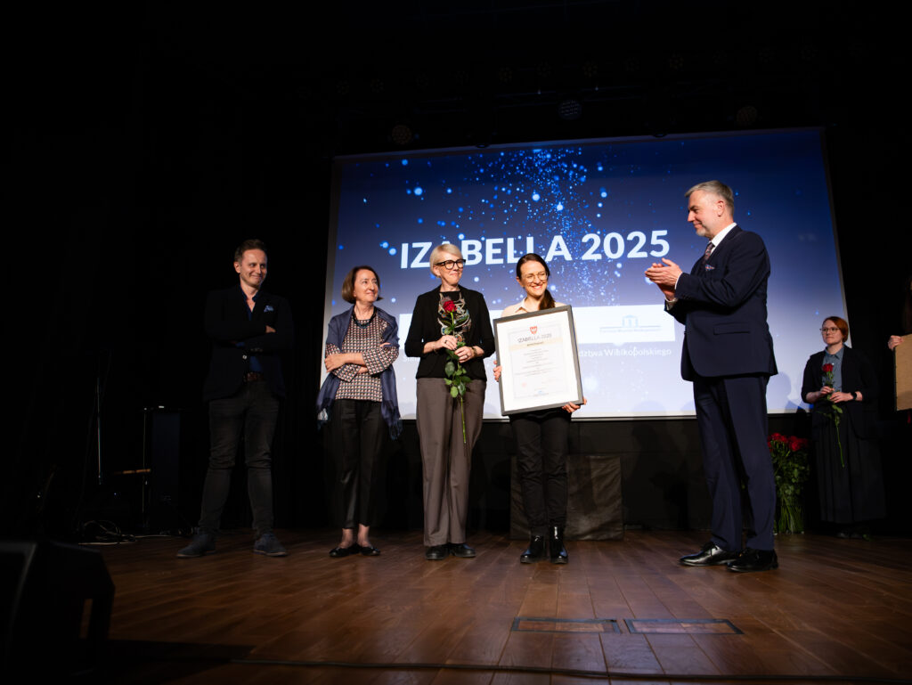 Zdjęcie kilku osób z dyplomem oprawionym w ramę. W tle ekran z wyświetlonym napisem Izabella 2025.