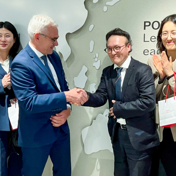 IMG_7273 Na pierwszym planie dyrektor Muzeum Narodowego w Poznaniu ściska rękę dyrektorowi Voc Sou Kim z Korei. Wokół nich kilka osób z delegacji. Stoją na tle mapy świata.
