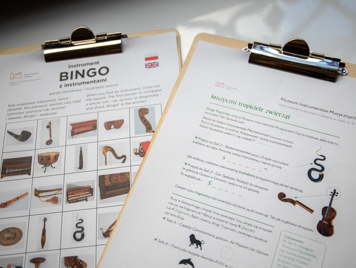 Dwie kartki papieru z zadaniami do wykonania. Na lewej kartce napis: Bingo z instrumentami. Na prawej kartce napis: Muzyczni tropiciele zwierząt.