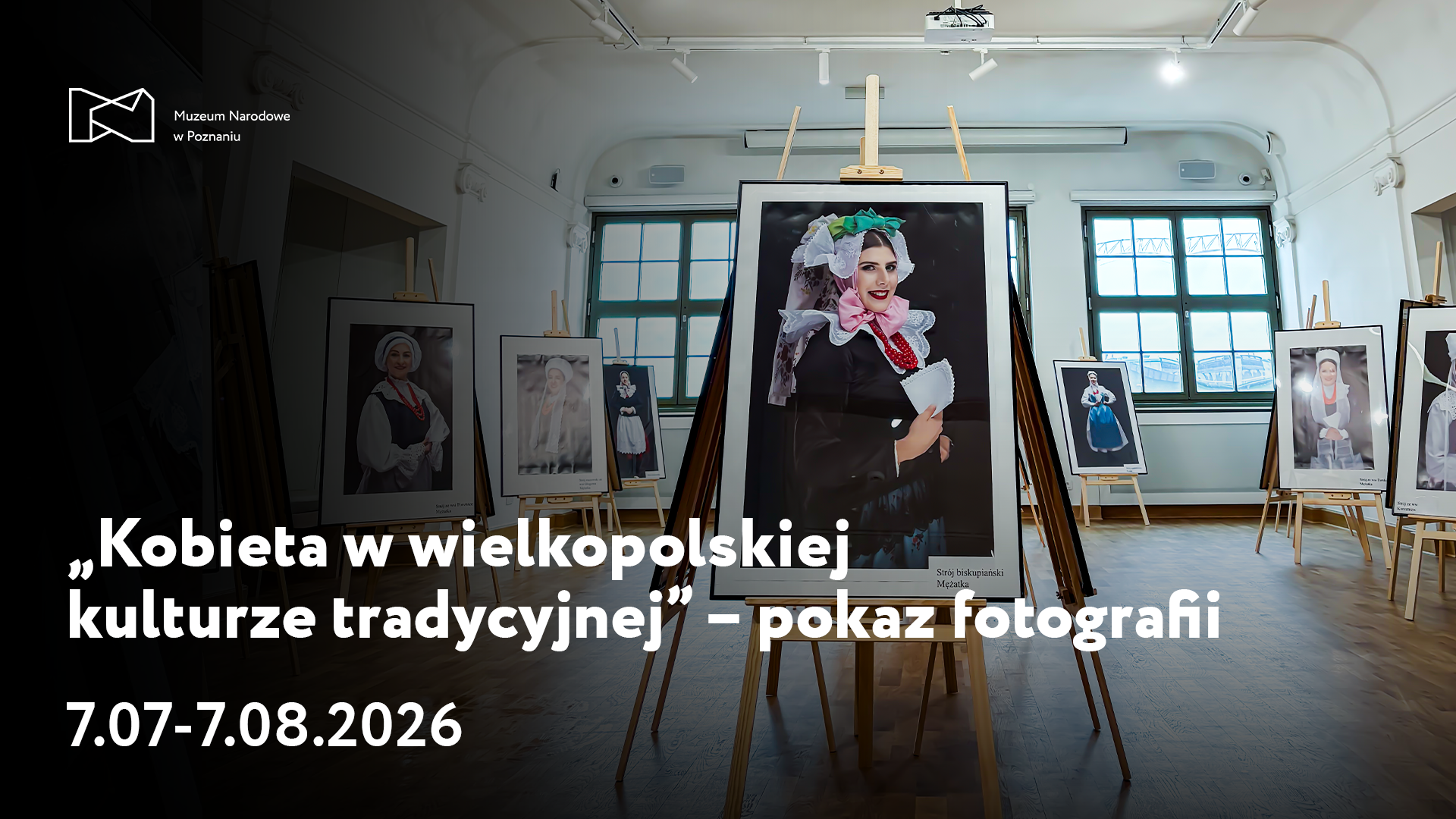 Afisz z napisem: Kobieta w wielkopolskiej kulturze tradycyjnej - pokaz fotografii. 7 lipca do 7 sierpnia 2026. W tle zdjęcie dużego pomieszczenia z ustawionymi na środku dużymi zdjęciami na sztalugach.